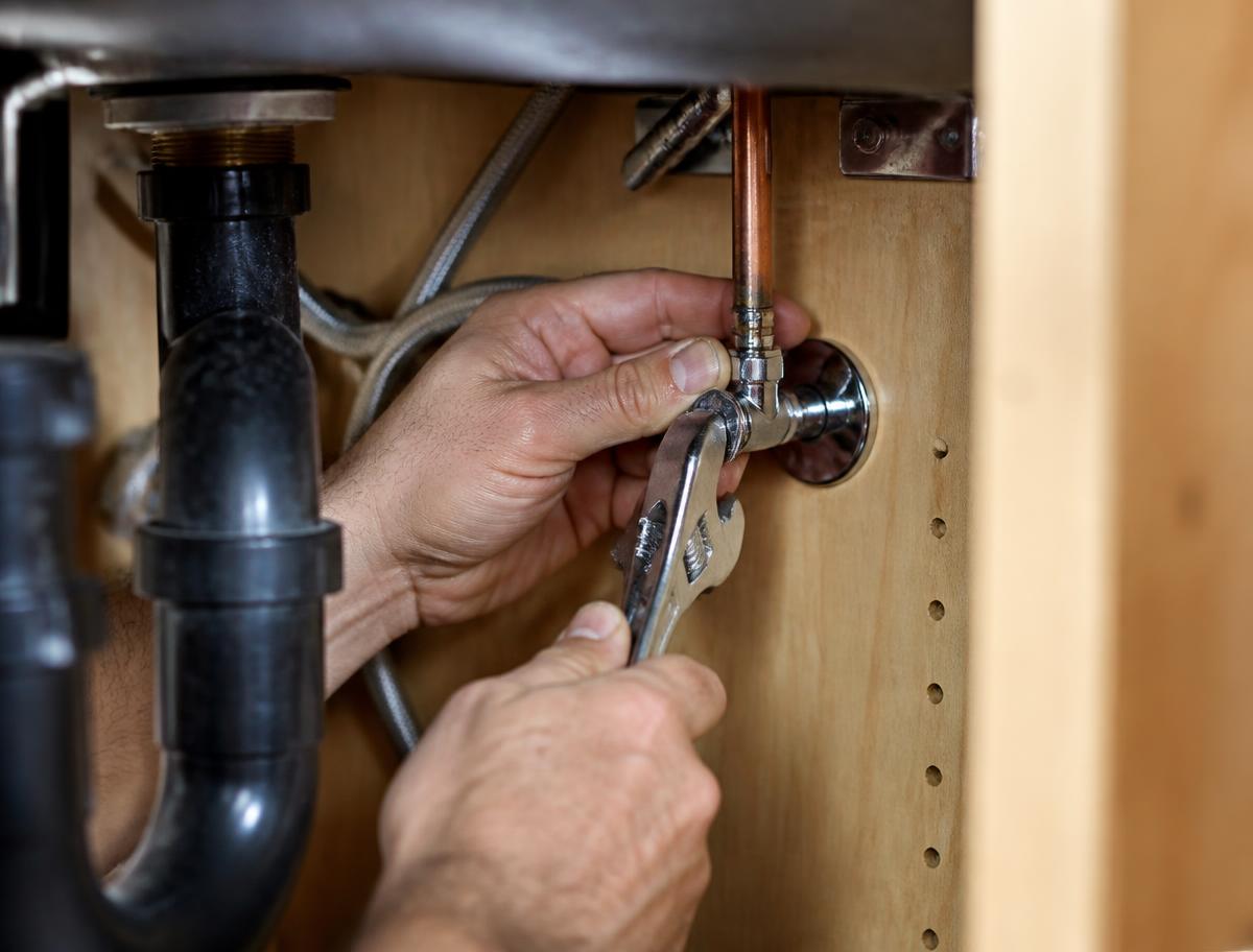 Plumber repairing a copper pipe under a sink with a wrench